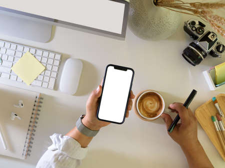 Top view of businessman holding smartphone and coffee cup while working on computer desk