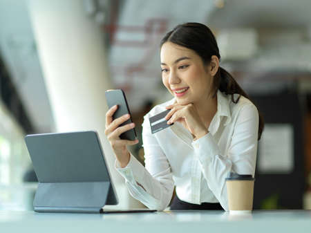Portrait of happy female office worker shopping on smartphone and online paying with credit card