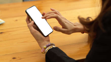 Cropped shot of businesswoman texting on smartphone with mock up screen on wooden table, clipping...