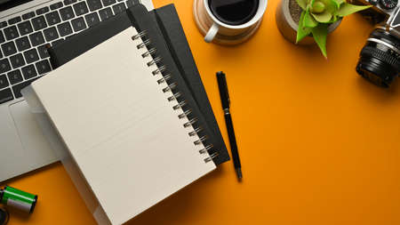 Top view of stylish workspace with notebooks, pen, laptop, camera, coffee cup and plant pot on...