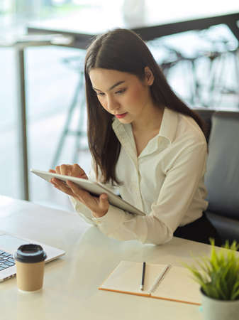 Portrait of busy female office worker concentrating on her work with digital tablet in her handの写真素材