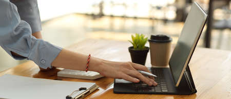 Side view of female office worker hand typing on tablet keyboard on office table with paperwork