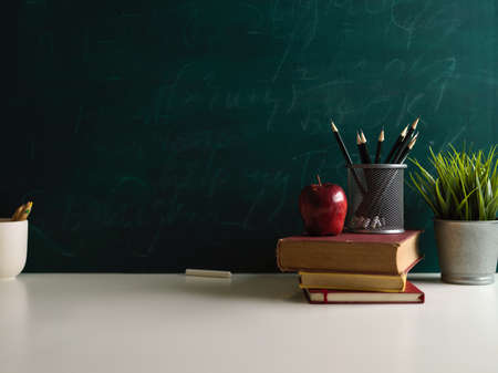 Close up view of books and school elements on study table in class room with chalkboard wall...
