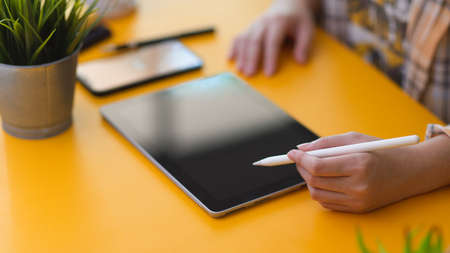 Close up view of female freelancer working on digital tablet with stylus pen on stylish workspace in...
