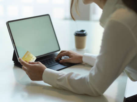 Side view of female online paying with debit card and digital tablet on white table in office room