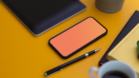 Close up view of smartphone with mock up screen on yellow table with stationery and coffee cupの写真素材