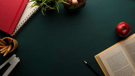 Top view of study table with book, stationery, notebook, supplies and copy space on dark green...