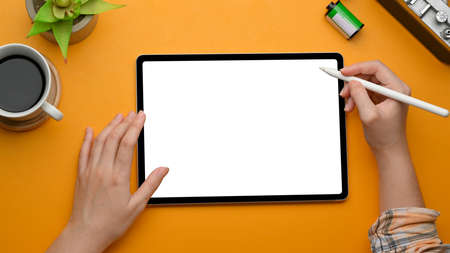 Top view of female hands using digital tablet with stylus pen on yellow  table, clipping path