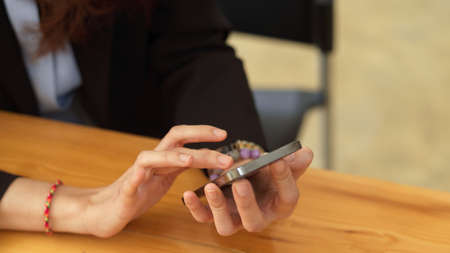 Close up view of female hand touching on smartphone screen while sitting at workplace