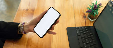 Side view of businesswoman in black suit holding mock up smartphone in her hand on office desk,...