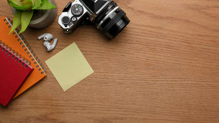 Top view of workspace with camera, notebooks, notepad, earphone and copy space on wooden tableの写真素材