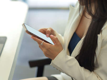Side view of businesswoman texting on smartphone while relax from work in workplaceの写真素材