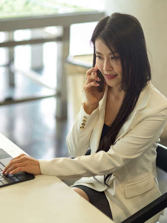 Cropped shot of businesswoman talking on the phone while working with laptop in office room