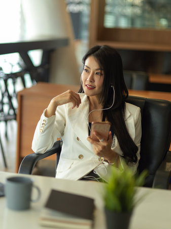 Portrait of businesswoman takes short time-out in office work using earphone and smartphone to relaxの写真素材