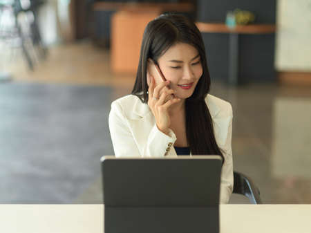Portrait of young businesswoman smiling and talking on the phone while sitting at workplaceの写真素材