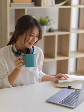 Cropped shot of female student relaxing with coffee while doing assignment in living room at homeの写真素材