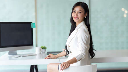 Portrait of businesswoman looking back and smiling to camera while sitting in modern office roomの写真素材