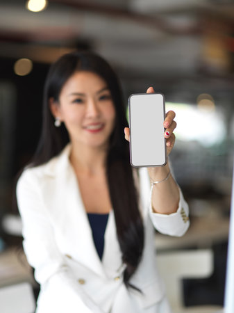 Portrait of businesswoman showing smartphone with mock up screen to camera in blurred background, clipping pathの写真素材