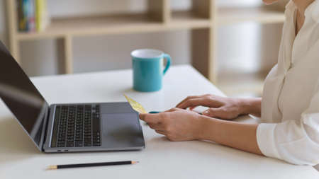 Side view of female hands holding credit card to online payment on smartphone while sitting at...