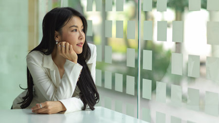 Portrait of businesswoman hand to cheek and enjoying the view from office glass wallの写真素材