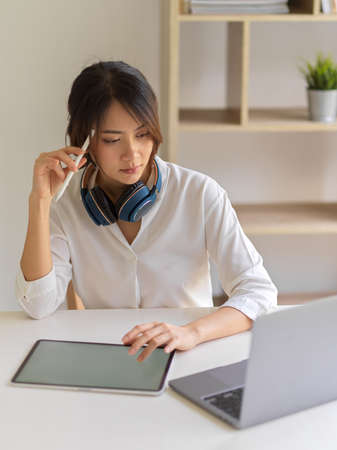 Portrait of female worker thinking about her work while using digital tablet and laptop in living roomの写真素材