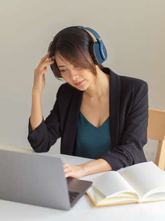 Portrait of businesswoman concentrating on her work while using headphone, laptop and book in office...