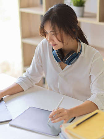 Portrait of female working with digital tablet and laptop on white desk in home office roomの写真素材