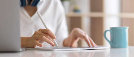 Close up view of female using digital tablet with stylus pen on the table in home office roomの写真素材