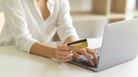 Cropped shot of female hand with credit card and typing on laptop keyboard while online shopping at homeの写真素材