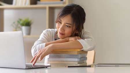 Close up view of female university student got tired of studying with stack of books and laptopの写真素材