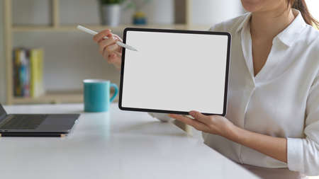 Female in white shirt presenting digital tablet with mock up screen and using stylus pointing on the screenの写真素材