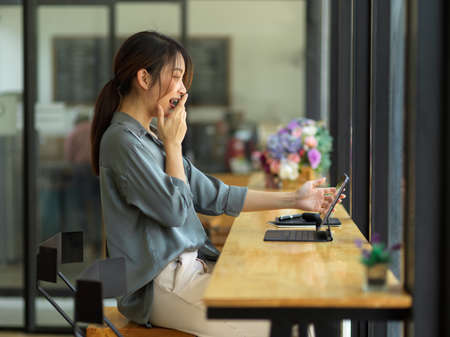 Side view of excited young female looking at digital tablet screen, feeling amazed while using digital tabletの写真素材