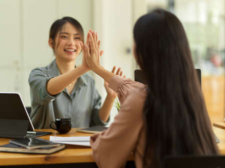 Portrait of two businesswomen celebrating and giving high fives during consulting on their projectの写真素材