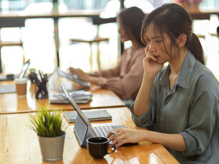 Side view of female office worker working with digital tablet in office room with her coworkerの写真素材