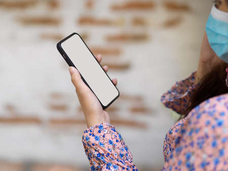 Side view of female in beautiful spring dress wearing medical mask and using smartphone in blurred background, clipping pathの写真素材