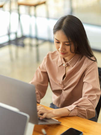 Cropped shot of young female office worker working with laptop on wooden table in comfortable office roomの写真素材