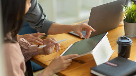 Side view of two businesswomen hands using digital tablet while briefing on their project on wooden tableの写真素材