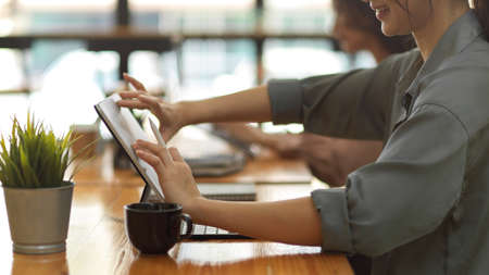 Side view of female worker hands touching on digital tablet screen while working in office roomの写真素材