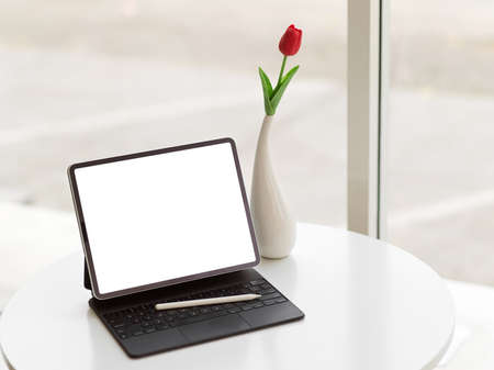 Cropped shot of portable workspace with digital tablet, accessories and flower vase on coffee table in cafeの写真素材