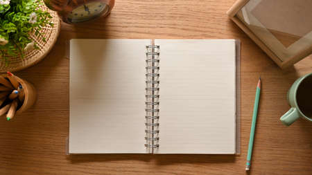 Top view of wooden workspace with opened blank notebook, pencils, cup and decorations in home office roomの写真素材