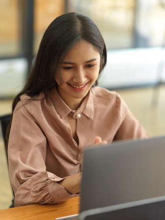 Portrait of beautiful businesswoman smiling while working with laptop in office roomの写真素材