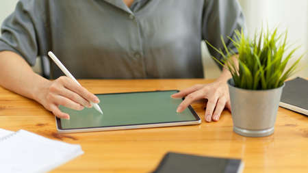 Close up view of female working on digital tablet with stylus pen on wooden office desk with office suppliesの写真素材