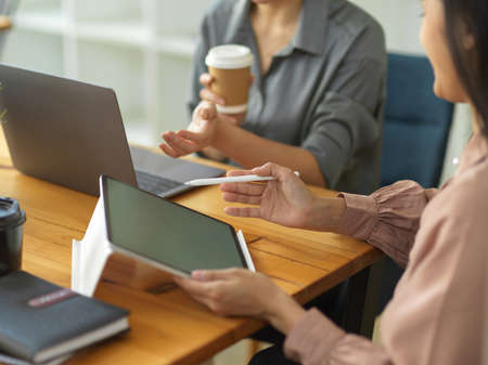Close up view of two businesswomen using digital tablet and laptop while sharing idea to each other in meeting roomの写真素材