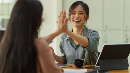 Close up view of two businesswomen celebrating and giving high fives during consulting on their projectの写真素材