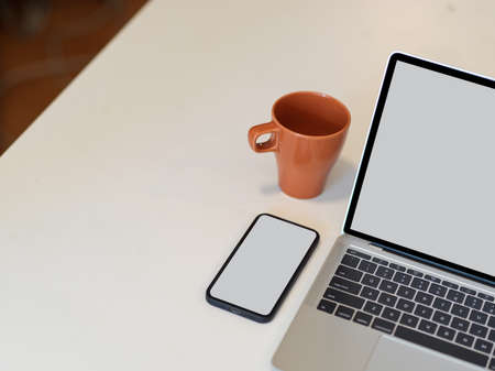 Cropped shot of white table with laptop, smartphone, mug and copy space in office room, clipping pathの写真素材