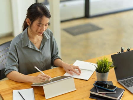 Portrait of businesswoman concentrating on her work with digital tablet and notebook on office deskの写真素材