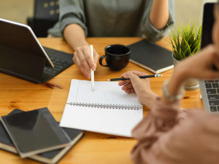 Close up view of two female workers working with stationery on wooden table in meeting room