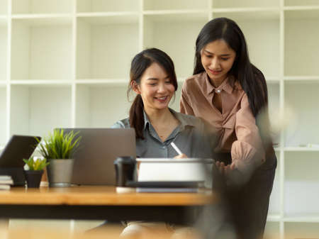 Two young businesswomen consulting on their work with office supplies in comfortable office roomの写真素材