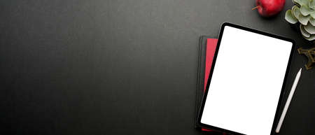 Top view of dark creative workspace with digital tablet, notebook, apple, plant pot and copy space, clipping pathの写真素材