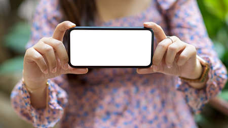 Cropped shot young female showing blank screen mock up smartphone to the camera, include clipping pathの写真素材